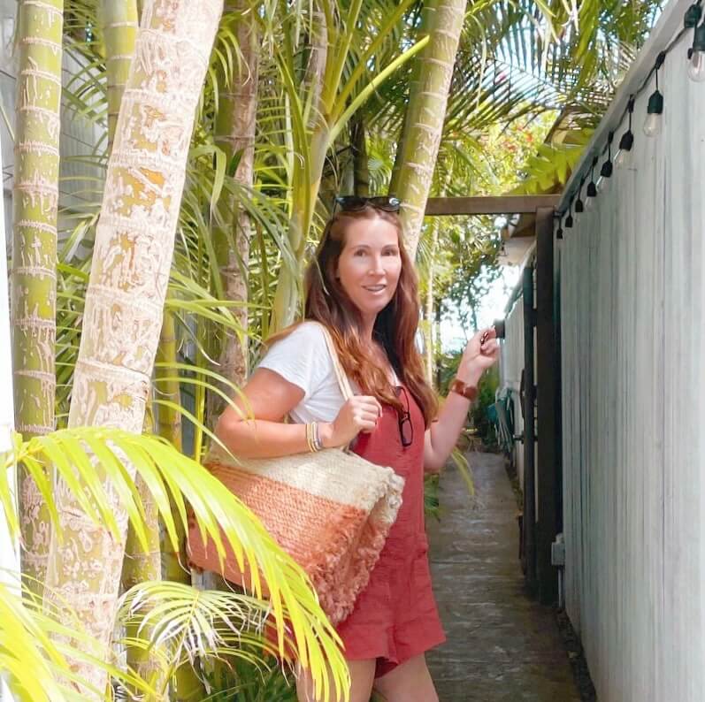 girl with bag next to palm tree pointing out to the beach.